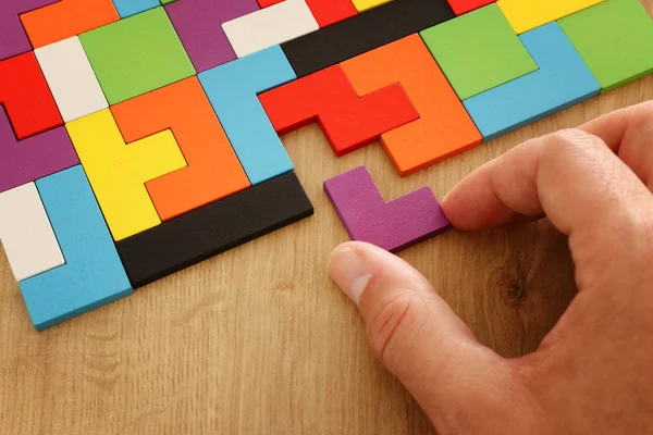 Mano dell'uomo che tiene un puzzle quadrato del tangram, sopra la tabella di legno — Foto Stock