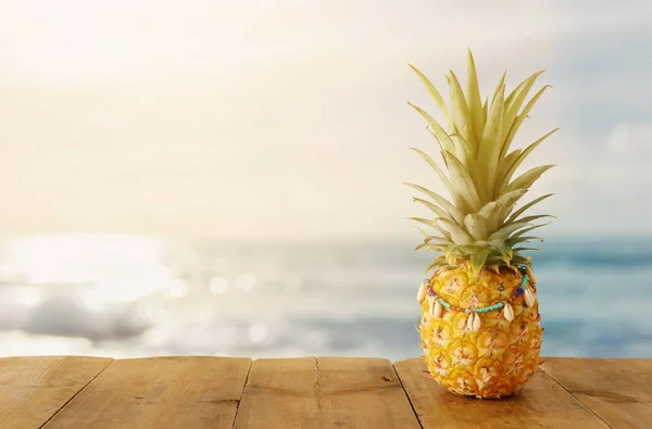 Ripe pineapple over wooden table in front of beach and tropical background — Stock Photo, Image