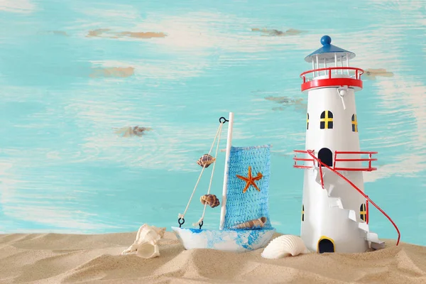 Vacances et concept d'été avec bateau vintage, étoile de mer, phare et coquillages sur la plage de sable devant fond bleu pastel — Photo