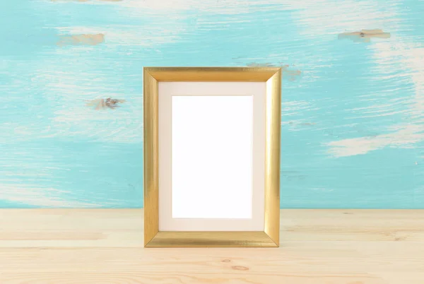 blank gold photo frame over wooden table and pastel blue background. Ready for photography montage
