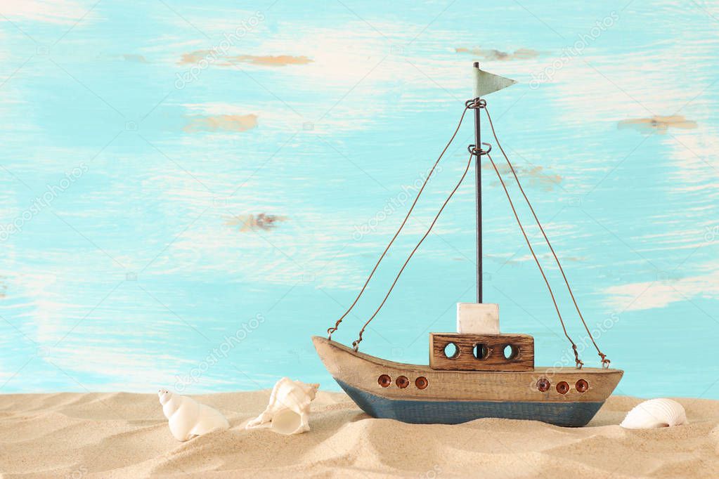 vintage wooden boat over beach sand and pastel blue background