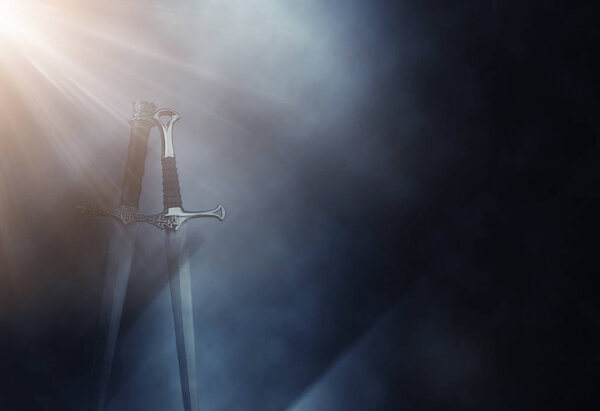 Mysterious and magical photo of silver sword over gothic black background with smoke. Medieval period concept