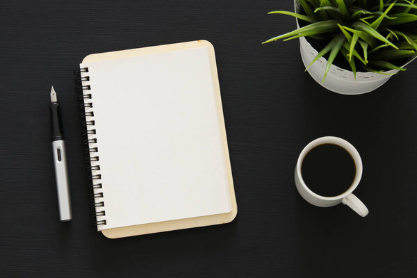 Open notebook with empty pages and other office supplies over black office desk table. Top view