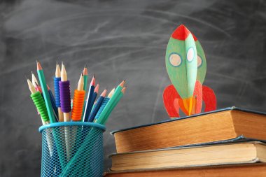 Okul konseptine geri dönelim. sınıf kara tahta önünde kitap üzerinde karton roket ve kalemler