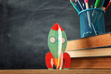 Okul konseptine geri dönelim. sınıf kara tahta önünde kitap üzerinde karton roket ve kalemler