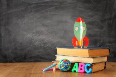 Okul konseptine geri dönelim. sınıf kara tahta önünde kitap üzerinde karton roket ve kalemler