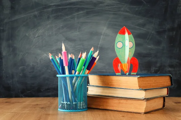 Вернемся к школьной концепции. картонная ракета и карандаши над книгами перед классной доской — стоковое фото