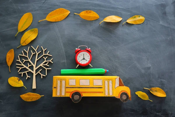 Вернемся к школьной концепции. Вид сверху на школьный автобус, будильник и карандаш рядом с деревом с осенью сухими листьями на фоне классной доски — стоковое фото