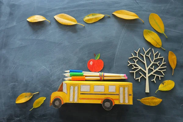 Torniamo al concetto di scuola. Vista dall'alto foto di cartone scuolabus, mela e matita accanto all'albero con autunno foglie secche su sfondo lavagna aula — Foto Stock