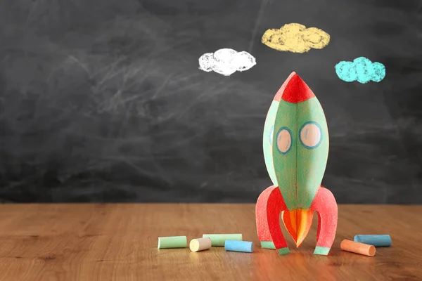 Education and back to school concept. cardboard rocket and chalks in front of classroom blackboard — Stock Photo, Image