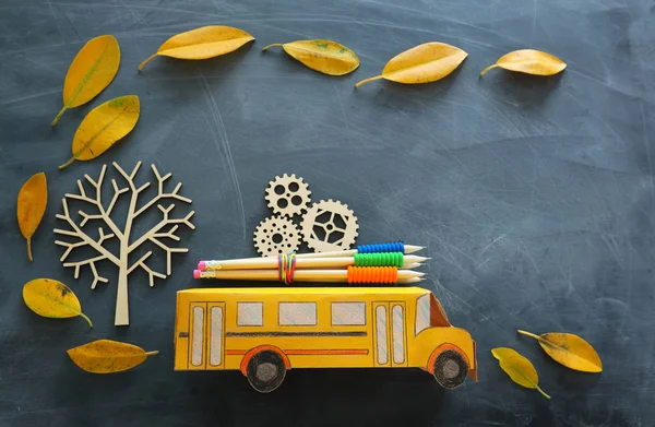 教育と学校の概念に戻る。段ボールスクールバスのトップビュー写真、成功と達成の概念として木製のギアと教室のブラックボアの上に秋の乾燥した葉を持つ木の隣に鉛筆 — ストック写真