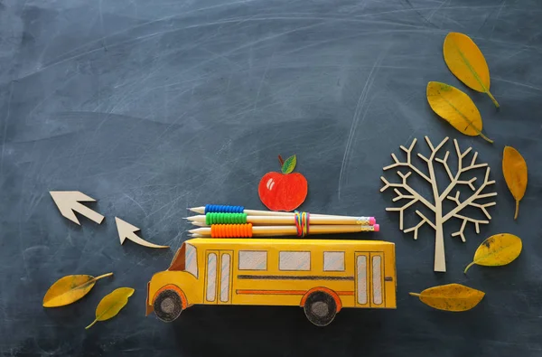 Educación y vuelta al concepto escolar. Foto de vista superior del autobús escolar de cartón, manzana y lápices al lado del árbol con hojas secas de otoño sobre el fondo de pizarra del aula — Foto de Stock