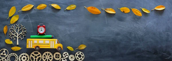 教育和回到学校的概念。纸板校车，闹钟和铅笔旁边的树与秋季干树叶在教室黑板背景的顶视图照片 — 图库照片