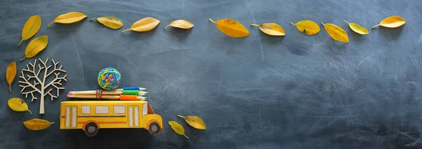 Éducation et concept de retour à l'école. Vue du dessus de l'autobus scolaire en carton et des crayons à côté de l'arbre avec des feuilles sèches d'automne sur le fond du tableau noir de la salle de classe — Photo