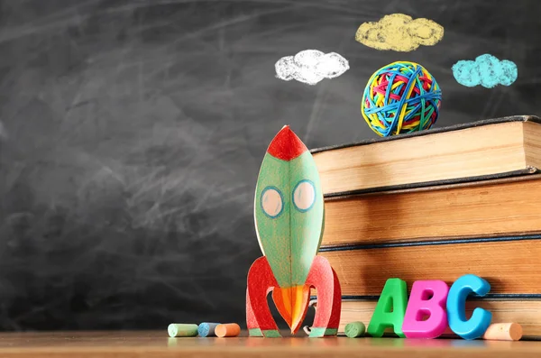 Education and back to school concept. cardboard rocket, books and chalks in front of classroom blackboard — Stock Photo, Image
