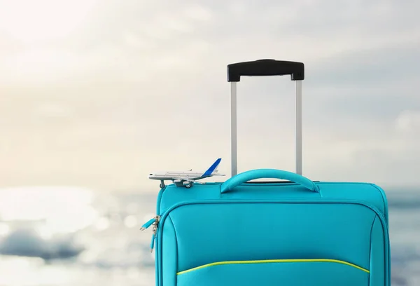 Feriados. conceito de viagem. mala azul e brinquedo de avião em frente ao fundo do mar tropical — Fotografia de Stock