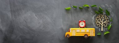 eğitim ve okul kavramına geri dön. Sınıf kara tahta arka plan üzerinde sonbahar yaprakları ile ağacın yanındaki çatıda okul otobüsü ve çalar saat üst görünüm fotoğrafı. üst görünüm, düz yatıyordu