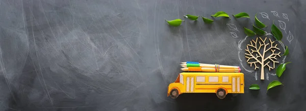 Образование и возврат к концепции школы. Фото школьного автобуса и карандашей на крыше рядом с деревом с осенними листьями на фоне классной доски. вид сверху, плоский — стоковое фото