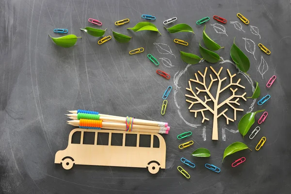 Образование и возврат к концепции школы. Вид сверху на деревянный автобус и карандаши на крыше рядом с деревом с осенними листьями на фоне классной доски. вид сверху, плоский — стоковое фото