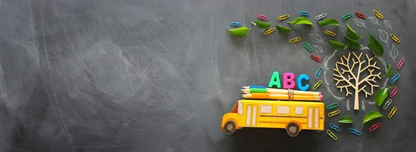 Образование и возврат к концепции школы. Фото школьного автобуса и букв ABC, карандашей на крыше рядом с деревом с осенними листьями на фоне классной доски. вид сверху, плоский — стоковое фото