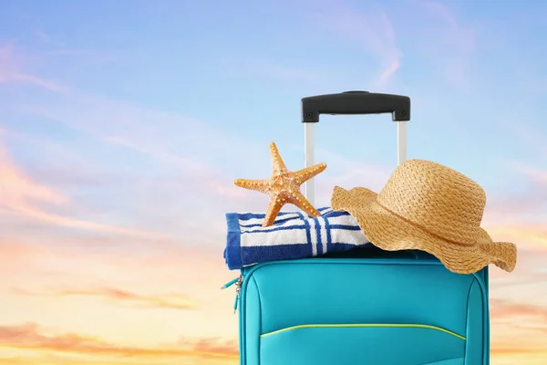 Feriados. conceito de viagem. mala azul com chapéu feminino, estrela do mar e toalha de praia em frente ao fundo tropical do céu por do sol — Fotografia de Stock