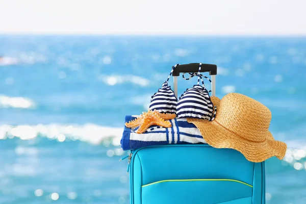 Праздники. концепция путешествия. голубой чемодан с женской шляпой, морской звездой, бикини и пляжным полотенцем перед тропическим фоном — стоковое фото
