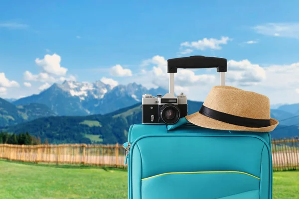 Obraz rekreacyjny bagażu podróżnego, kamery i kapelusza Fedora Infront wiejskiego lanscape. koncepcja wakacji i wakacji — Zdjęcie stockowe
