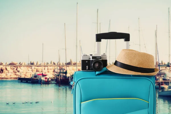 Imagen recreativa del equipaje del viajero, cámara y sombrero fedora frente al puerto deportivo con fondo de yates. vacaciones y concepto de vacaciones —  Fotos de Stock