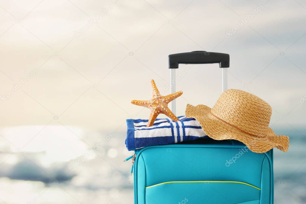 holidays. travel concept. blue suitcase with female hat, starfish and beach towel in front of tropical background