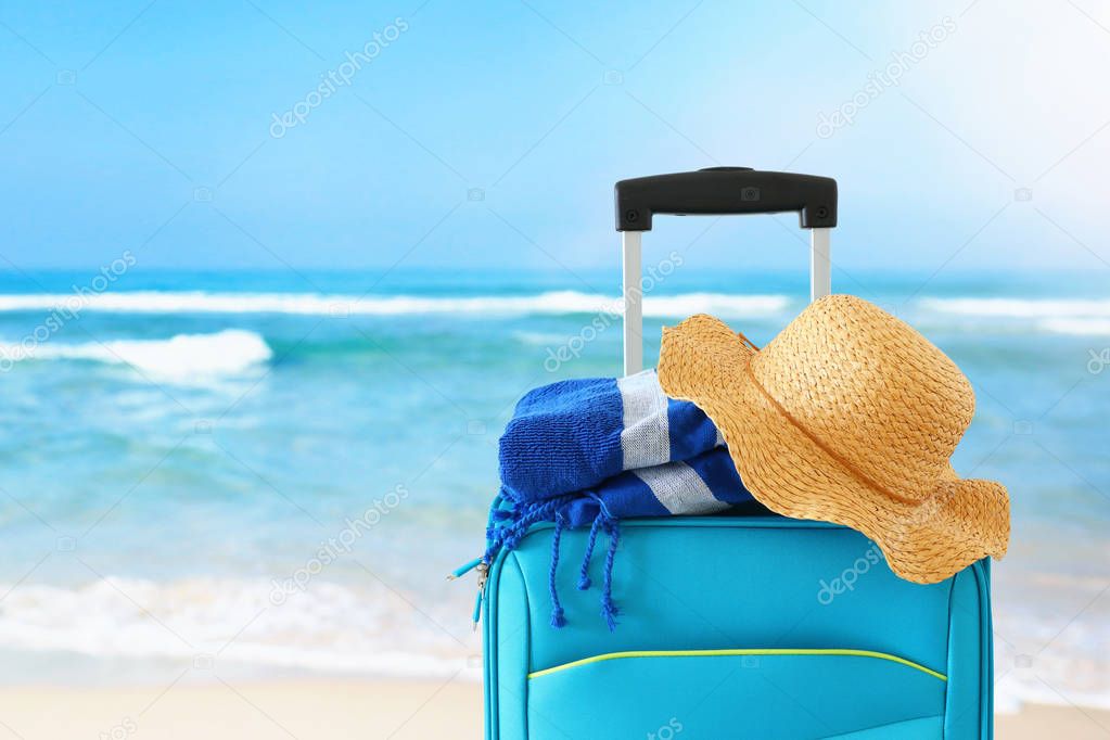 holidays. travel concept. blue suitcase with female hat and beach towel infront of tropical background