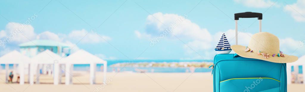 holidays. travel concept. blue suitcase with female hat and sailing boat infront of tropical background. banner
