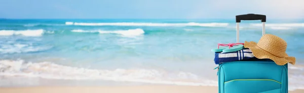 Holidays. travel concept. blue suitcase with female hat, flipflops in front of tropical marina background — Stock Photo, Image