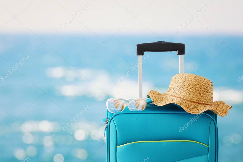 holidays. travel concept. blue suitcase with female hat, sunglasses in front of tropical background