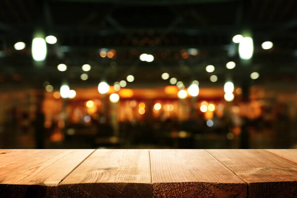 Изображение деревянного стола перед размытыми огнями ресторана