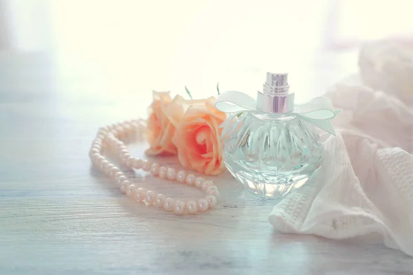 Belleza / moda Imagen de una elegante botella de perfume, perlas blancas y delicadas rosas sobre fondo pastel. vintage imagen filtrada — Foto de Stock