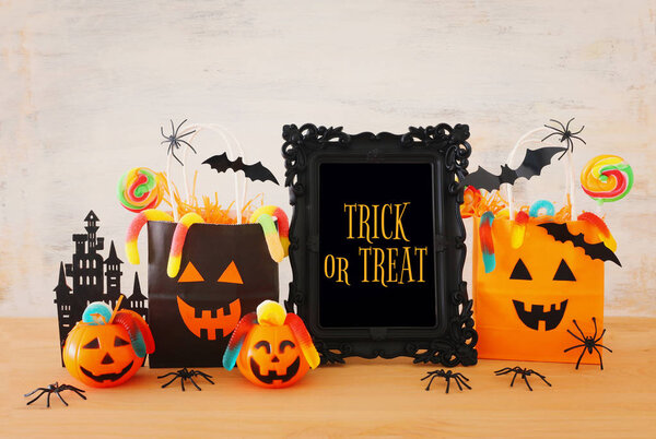 holidays image of Halloween. Pumpkins, bats, treats, paper gift bag over wooden table