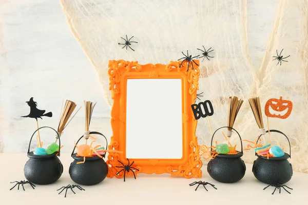 Vacaciones imagen de Halloween. Caldero de bruja, escoba, caramelos y arañas junto al marco de fotos vacío para maqueta sobre mesa de madera. para montaje fotográfico — Foto de Stock