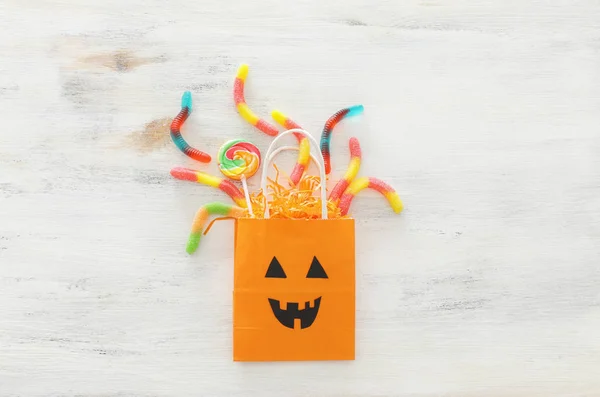 Urlaub Bild von halloween. Papiergeschenktüte und Süßigkeiten über einem weißen Holztisch. Draufsicht, flache Lage — Stockfoto