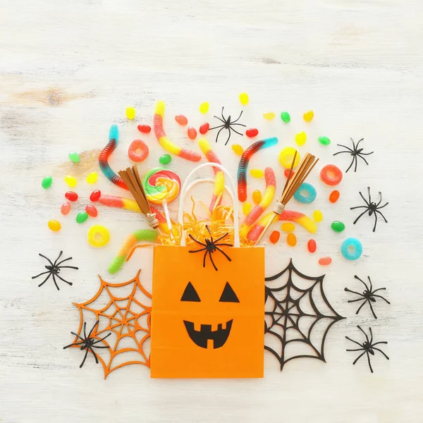 Vacaciones imagen de Halloween. bolsa de regalo de papel, araña, murciélagos y dulces sobre una mesa blanca de madera. vista superior, plano — Foto de Stock