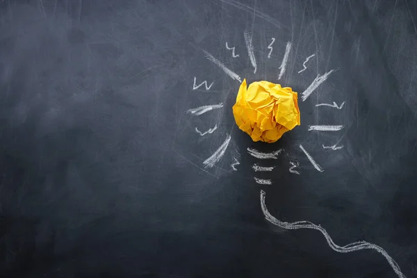 Education concept image. Creative idea and innovation. Crumpled paper as lightbulb metaphor over blackboard