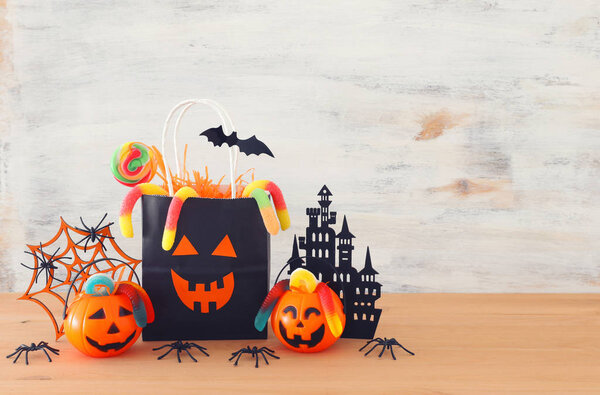 holidays image of Halloween. Pumpkins, bats, treats, paper gift bag over wooden table