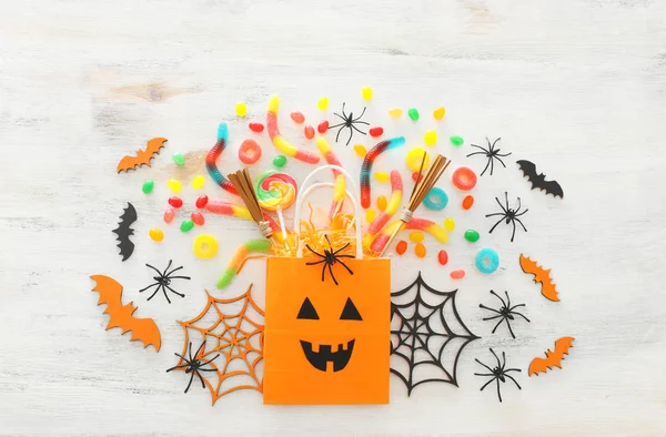 Urlaub Bild von halloween. Papiergeschenktüte, Spinne, Fledermäuse und Süßigkeiten über einem weißen Holztisch. Draufsicht, flache Lage — Stockfoto