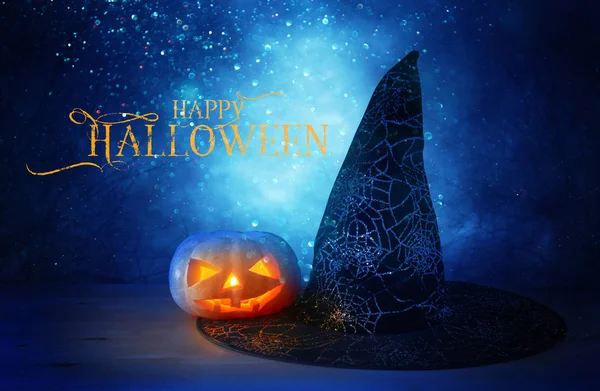 Concepto de vacaciones de Halloween. Sombrero de calabaza y bruja sobre mesa de madera en la noche bosque aterrador, embrujado y brumoso —  Fotos de Stock