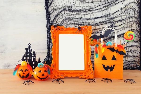 Vacaciones imagen de Halloween. Calabazas, murciélagos, golosinas, bolsa de regalo de papel junto al marco de fotos vacío para maqueta sobre mesa de madera. para montaje fotográfico — Foto de Stock