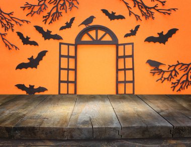 holidays concept of Halloween. Empty rustic table in front of open window and bats over orangr background. Ready for product display montage