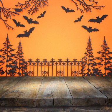 Cadılar bayramı konsepti. Perili sokağın önündeki boş kır masasında turuncu arka planda ağaçlar ve yarasalar var. Ürün görüntüleme kurgusu için hazır