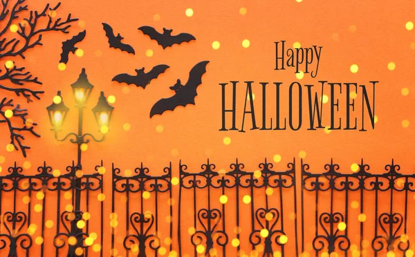 Feiertags-Halloween-Konzept. Gespenstergasse mit Vintage-Zaun, Straßenlaternenbäumen und Fledermäusen vor orangefarbenem Hintergrund. Draufsicht, flache Lage — Stockfoto