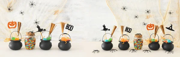 Vacaciones imagen de Halloween. Caldero de bruja, escoba, caramelos y arañas sobre mesa de madera blanca — Foto de Stock