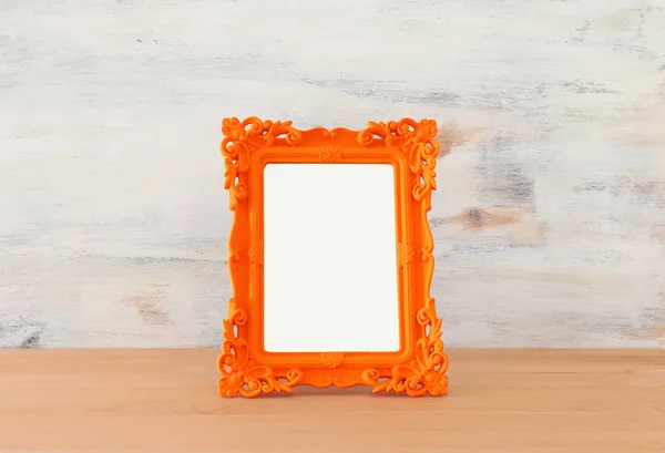 Pusta pomarańczowa ramka na drewnianym stole i białym tle. Gotowy do montażu fotografii — Zdjęcie stockowe