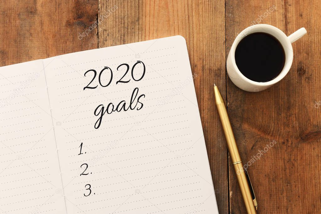 Business concept of top view 2020 goals list with notebook, cup of coffee over wooden desk